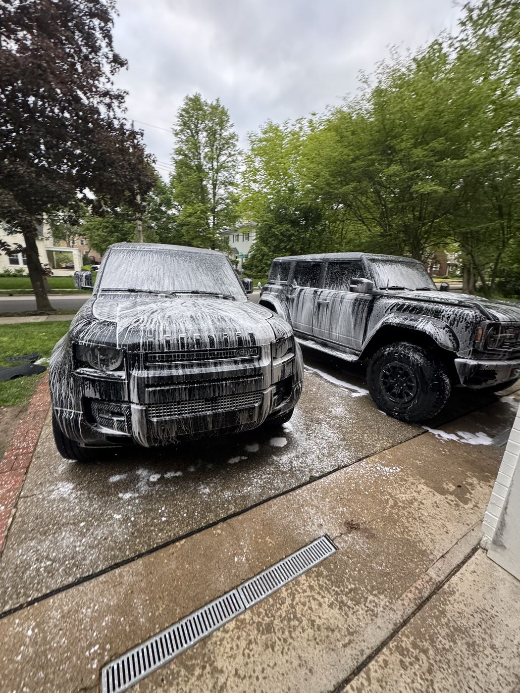 Land Rover Defender and Ford Bronco covered in wash foam on a driveway
